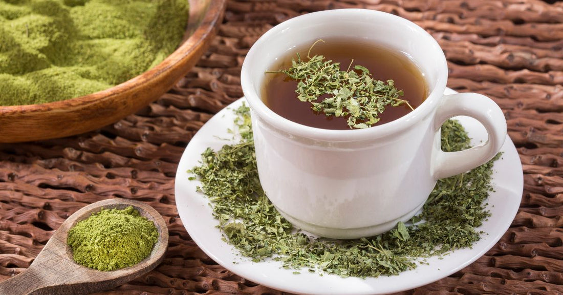 A cup of moringa tea with a tea bag beside it, accompanied by a spoonful of moringa powder, highlighting the benefits of this superfood infusion