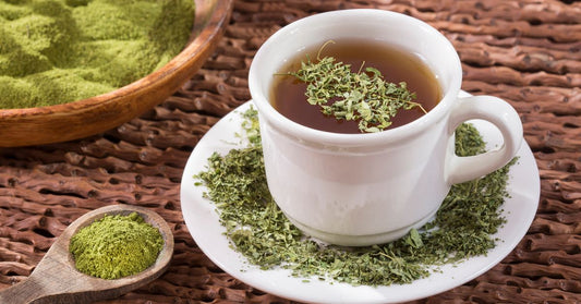 A cup of moringa tea with a tea bag beside it, accompanied by a spoonful of moringa powder, highlighting the benefits of this superfood infusion