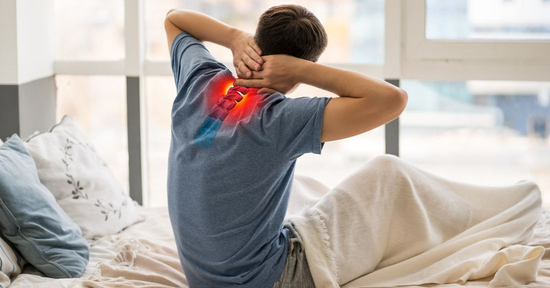 A man seen from behind getting out of bed in the morning, holding his lower back in pain, illustrating symptoms of spinal osteoarthritis