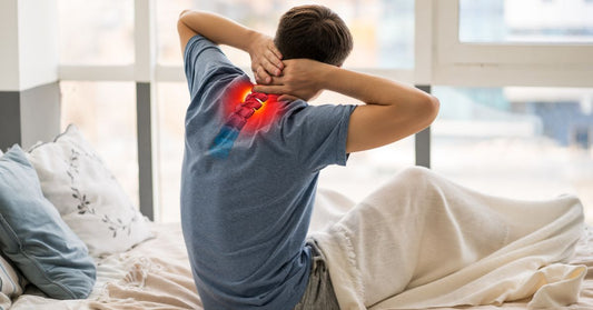 A man seen from behind getting out of bed in the morning, holding his lower back in pain, illustrating symptoms of spinal osteoarthritis