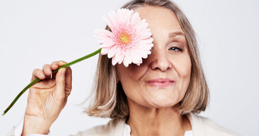 A smiling elderly woman holding a pink flower, symbolizing vitality and natural balance during perimenopause