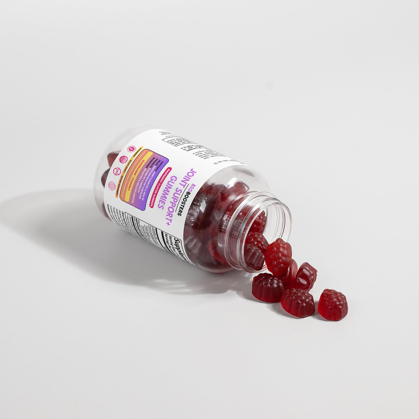 Bottle of gummy vitamins with a few gummies spilling out on a light gray background